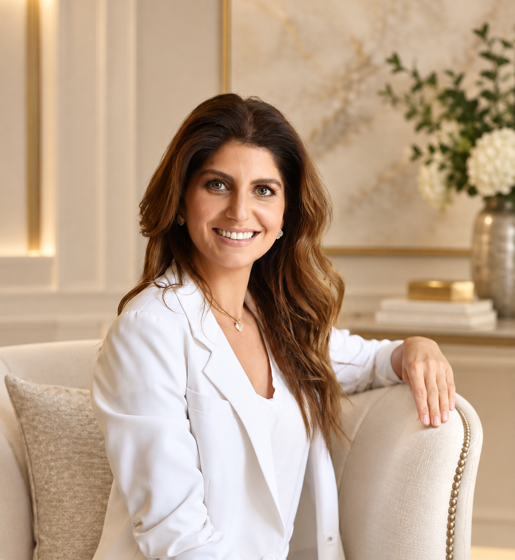 Sherri Ghodsian seated in a warm, elegant interior, smiling in a white blazer